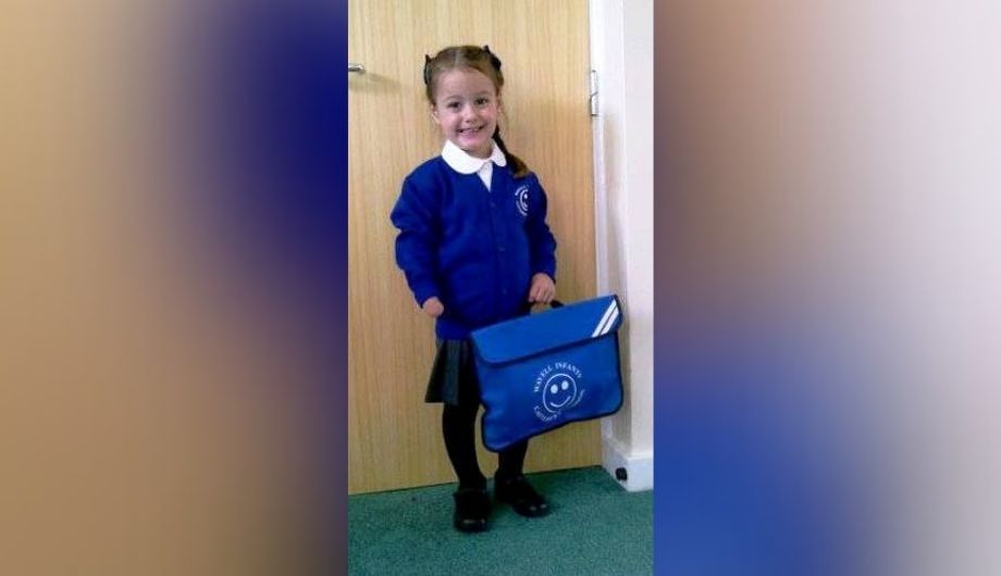 A young girl wearing a blue school uniform smiling.