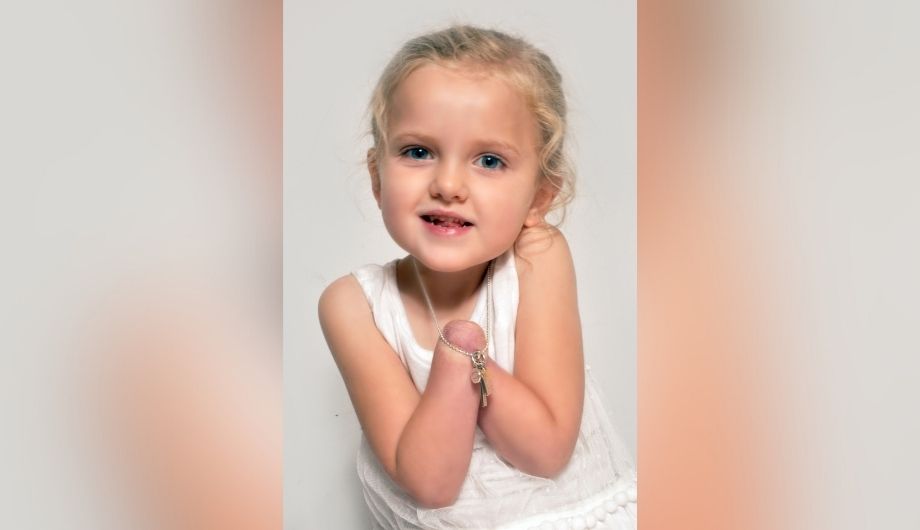 A young girl with limb loss smiling and holding a necklace.