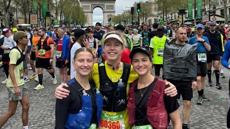 Three women in running outfits standing in front of the Arc de Triomphe.