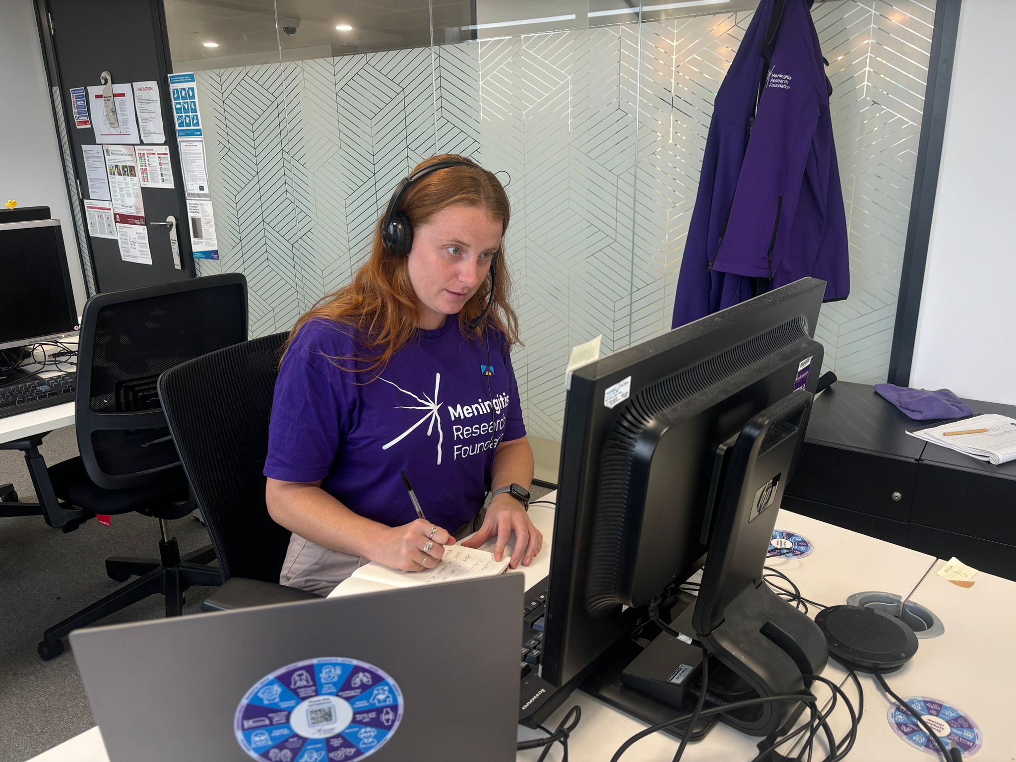Person speaks on the phone at a desk wearing a Meningitis Research Foundation t-shirt.