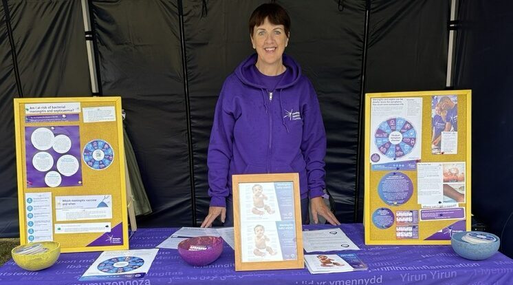 Woman wearing purple stood behind a stall with a purple table cloth and various materials on the table.