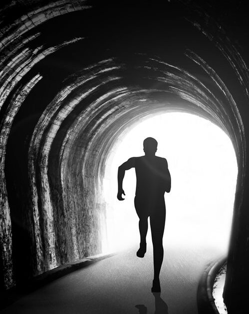 A black and white image of a silhouette of a man running in a tunnel.