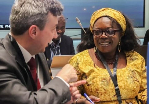 A man and a woman having a conversation at a conference. The man is gesticulating and the woman is smiling at him.