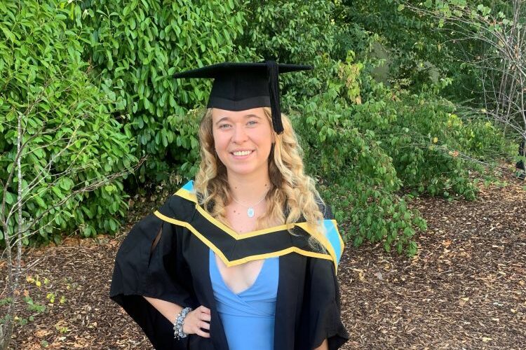 Ella Bailey smiling in her graduation cap and gown wearing a blue dress