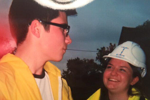 A photograph of two people smiling at each other, one is wearing a hard hat