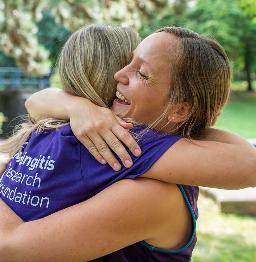 A woman smiling and hugging someone who is wearing a Meningitis Research Foundation t-shirt.