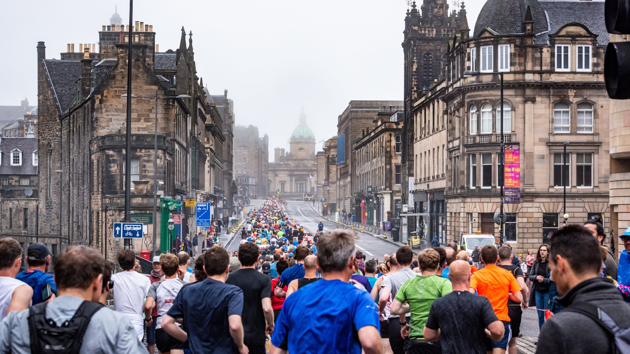 Group of people running up the Royal Mile in Edinburgh in misty weather.