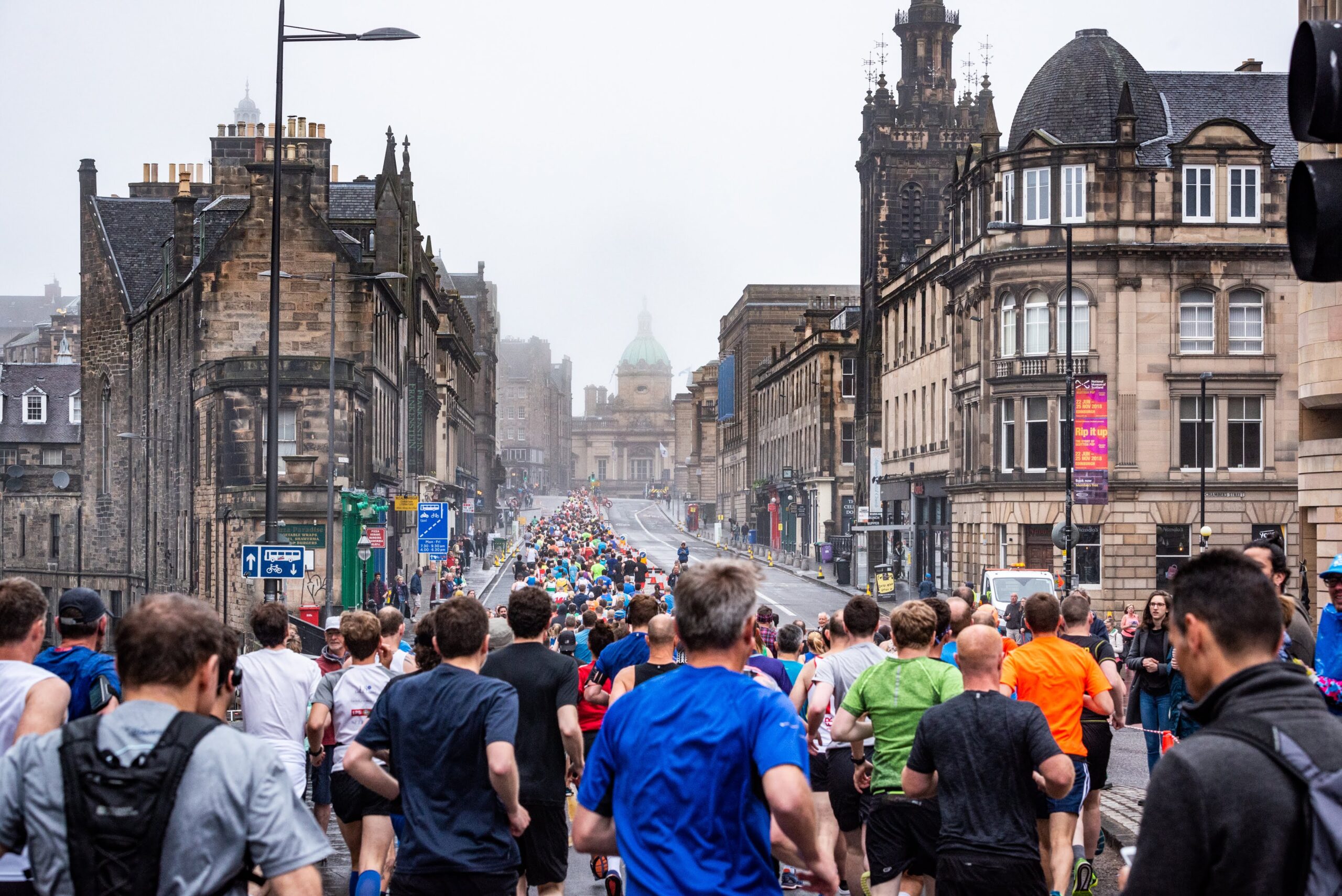 Group of people running up the Royal Mile in Edinburgh in misty weather.
