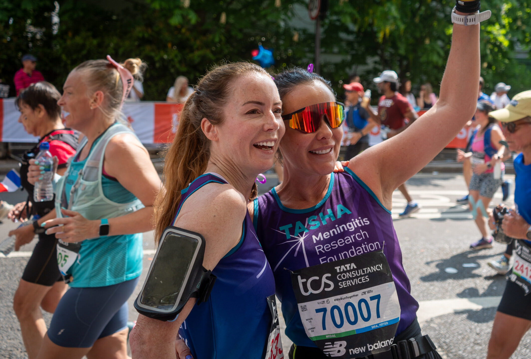 Two women running a marathon greeting someone in a crowd.