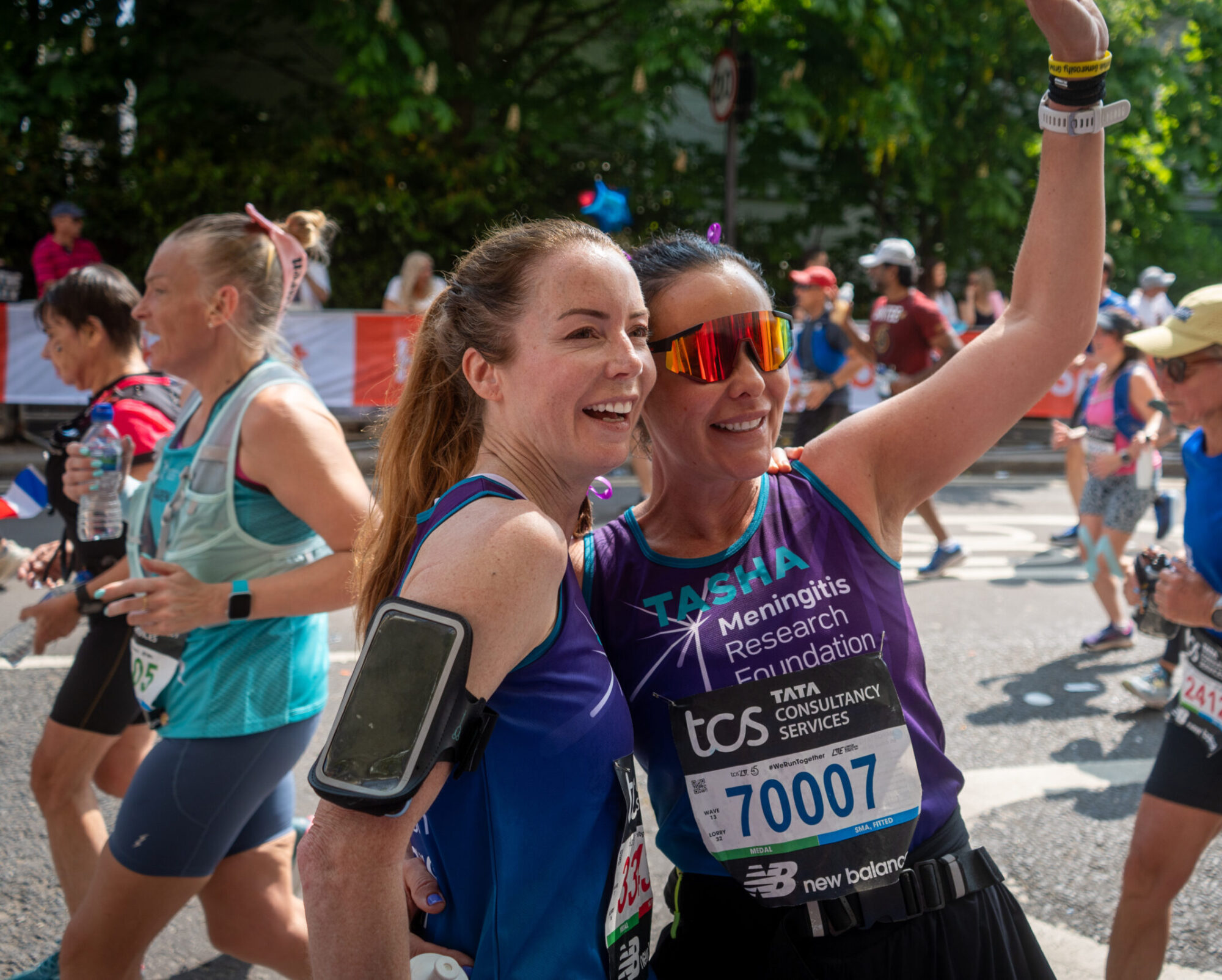 Two women running a marathon greeting someone in a crowd.