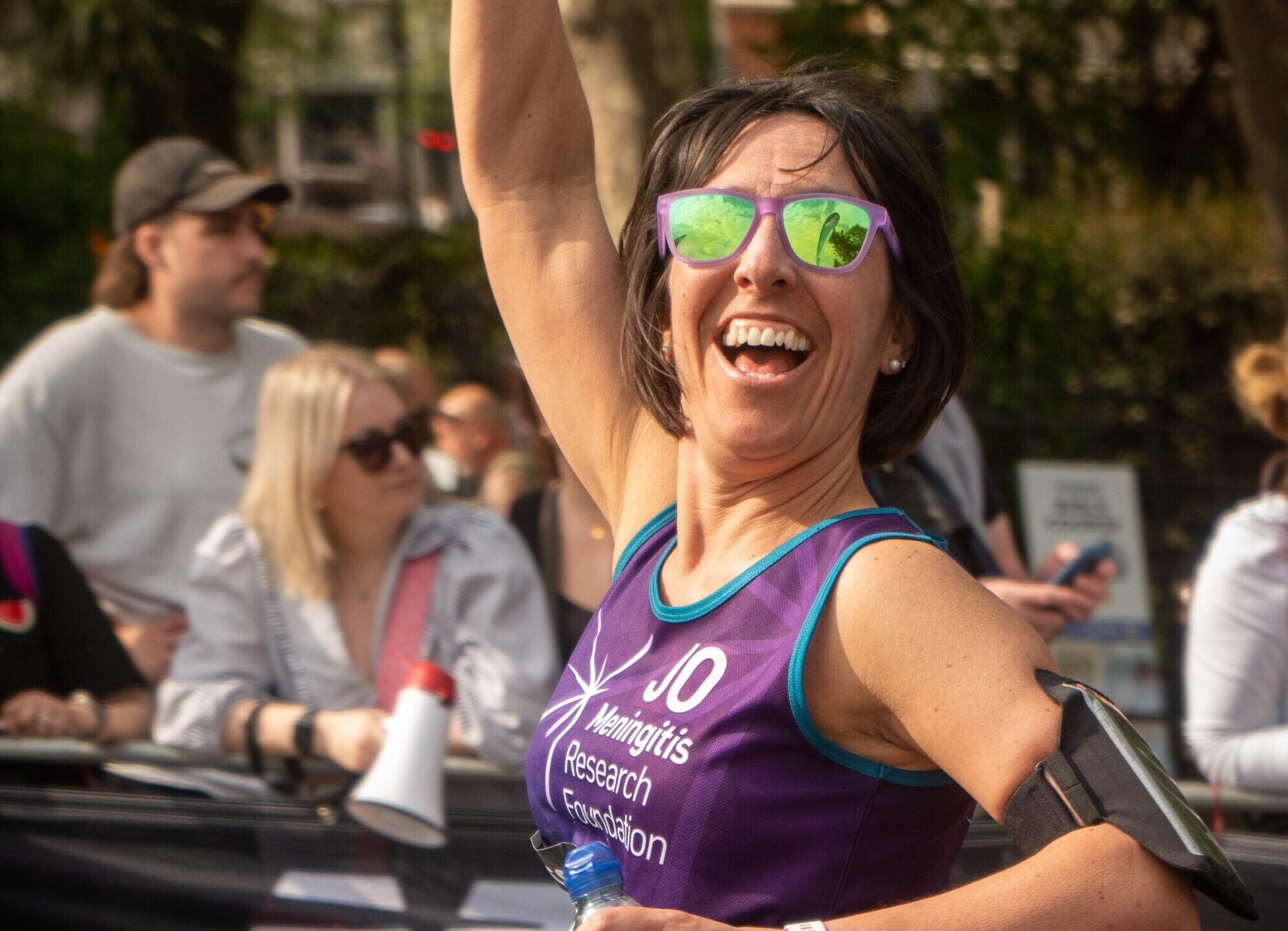 London Marathon runner with sunglasses waves in the air towards the camera.