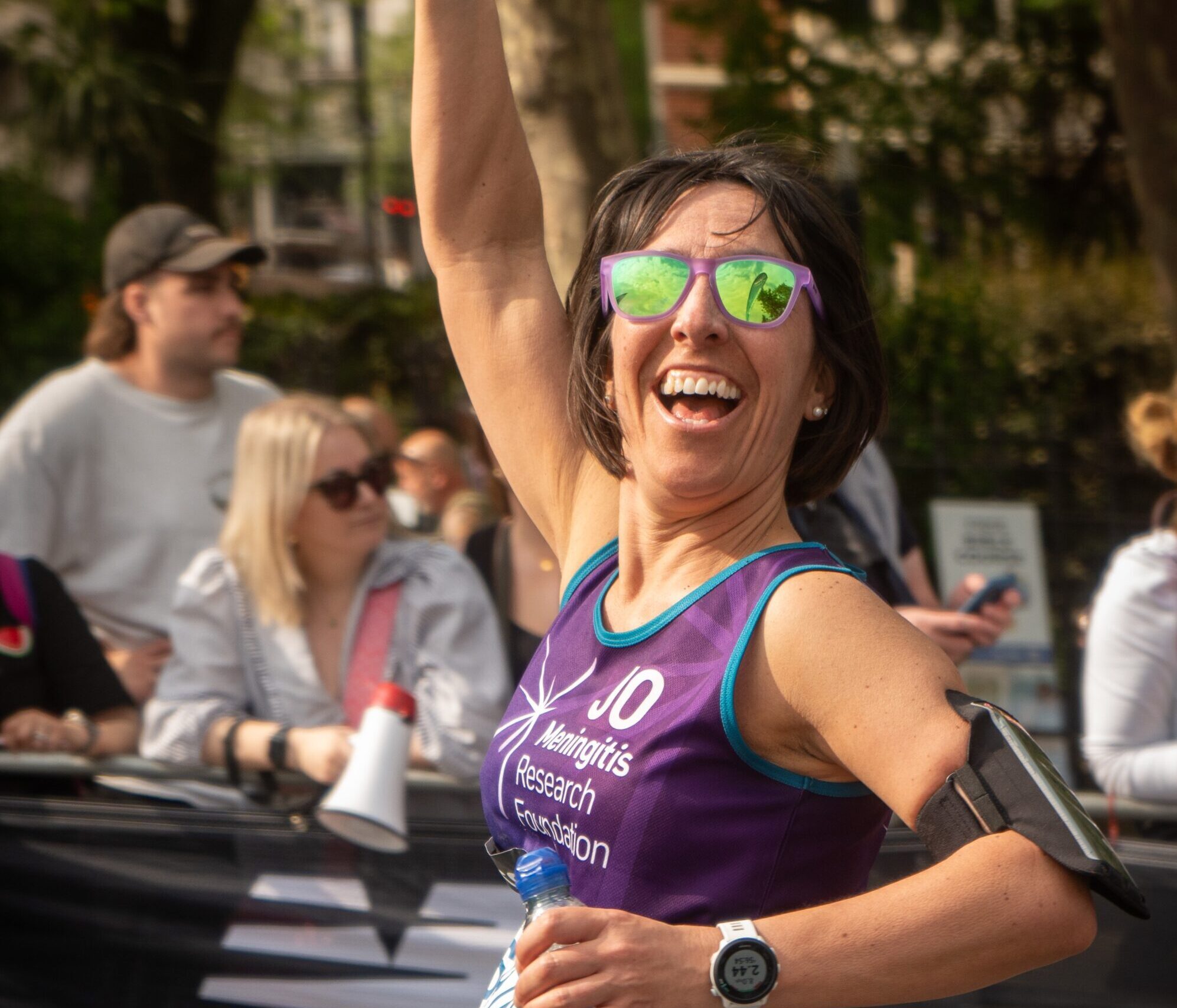 London Marathon runner with sunglasses waves in the air towards the camera.