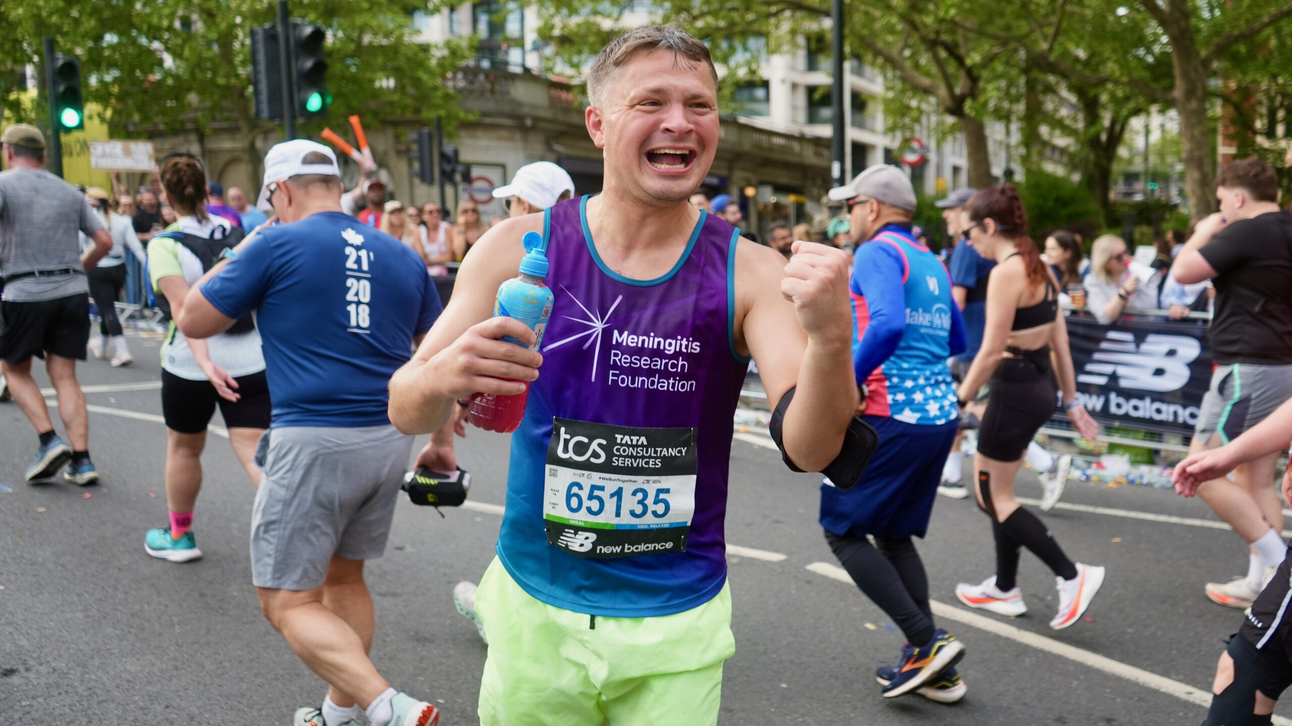 A London Marathon runner punches the air with joy.