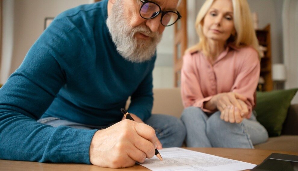 Image of man with a beard and glasses completing paperwork with a woman sitting beside him.