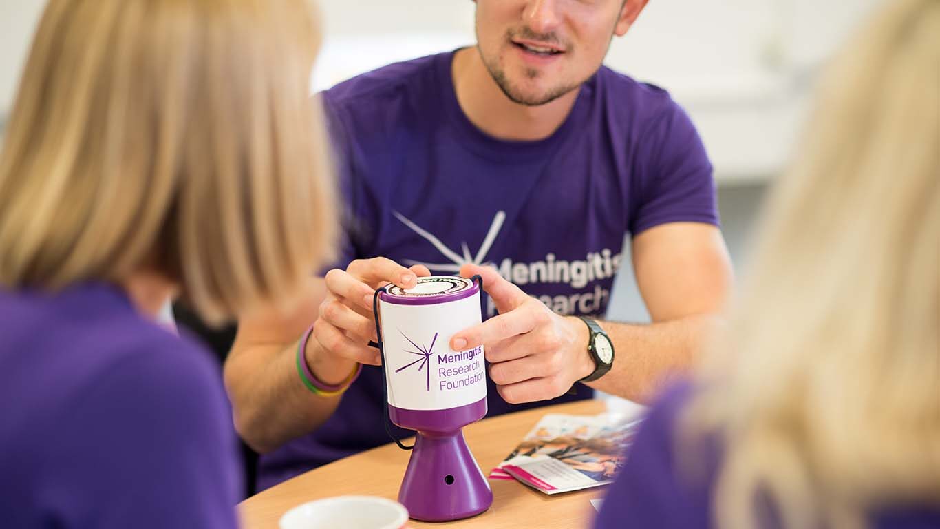 Man in Meningitis Research Foundation t-shirt holds collection tin.