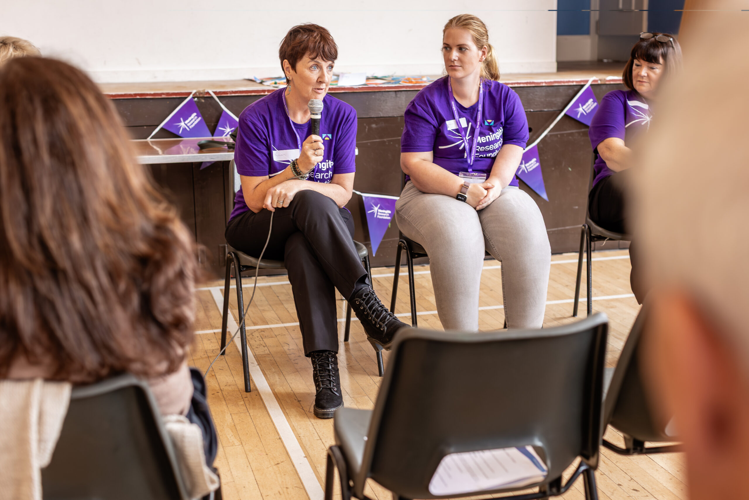 Two women sat at the front of a room, one is holding a microphone and speaking