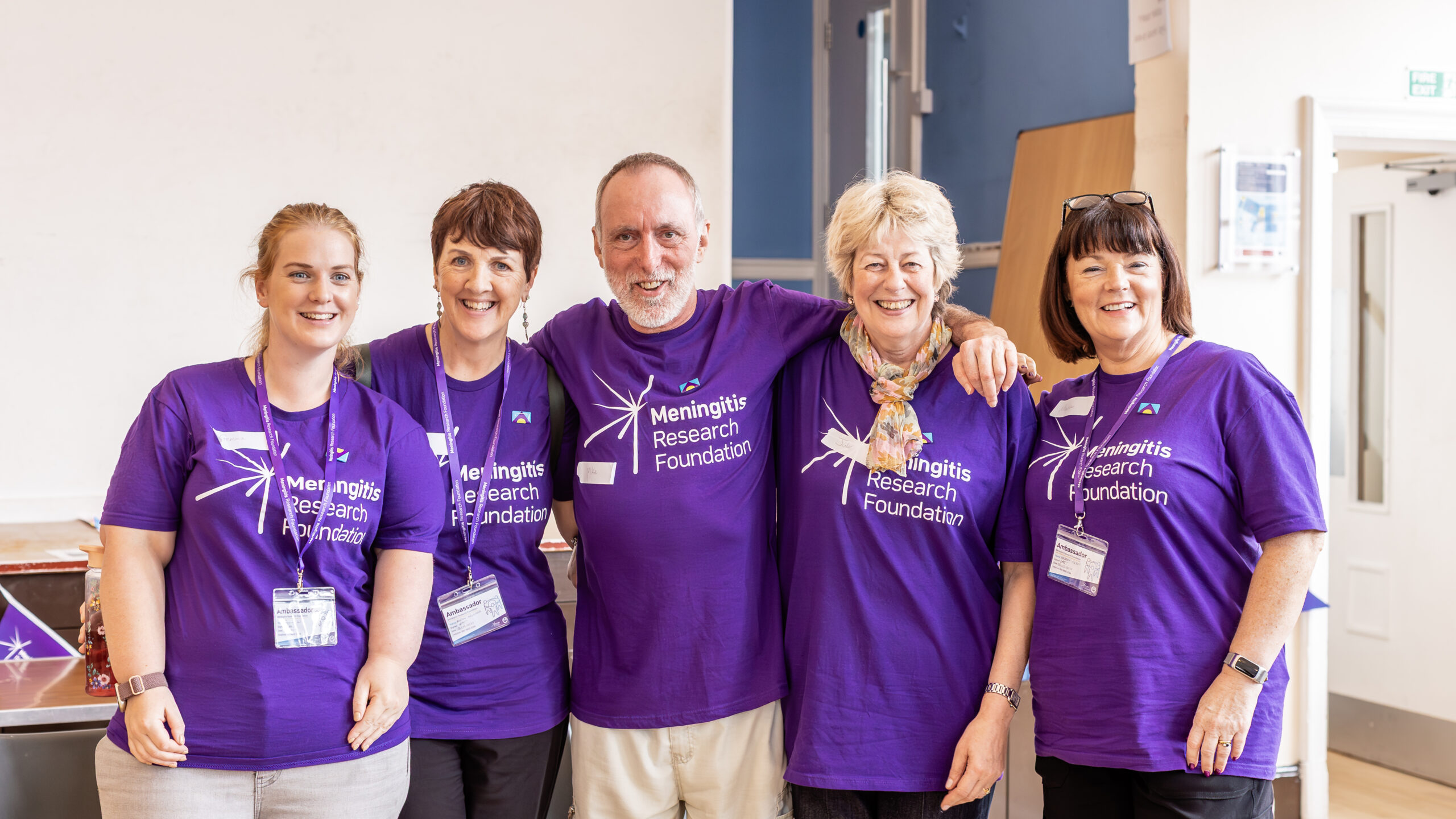 Five Meningitis Research Foundation Ambassadors stand together in their purple branded t-shirts.