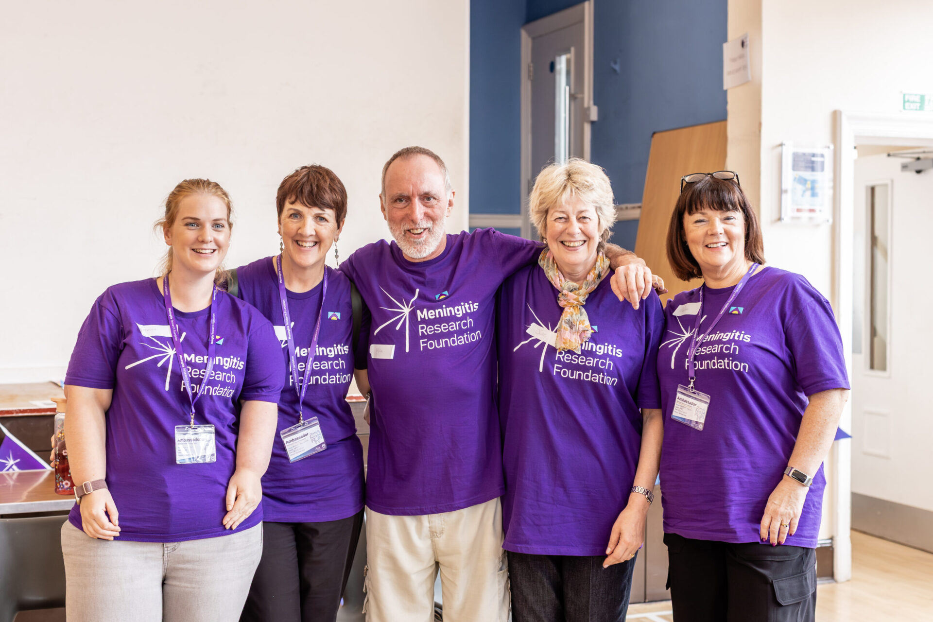 Five Meningitis Research Foundation Ambassadors stand together in their purple branded t-shirts.