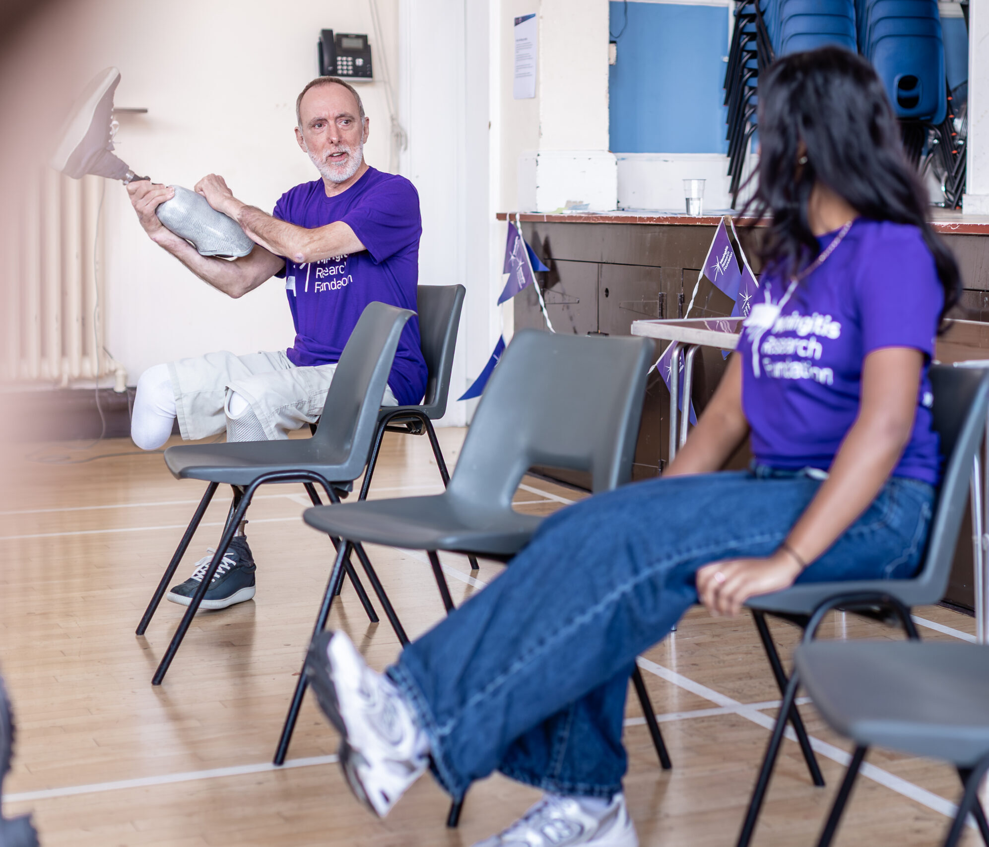 Man with prosthetic leg holding it up as part of a seated exercise session with the female instructor in the foreground
