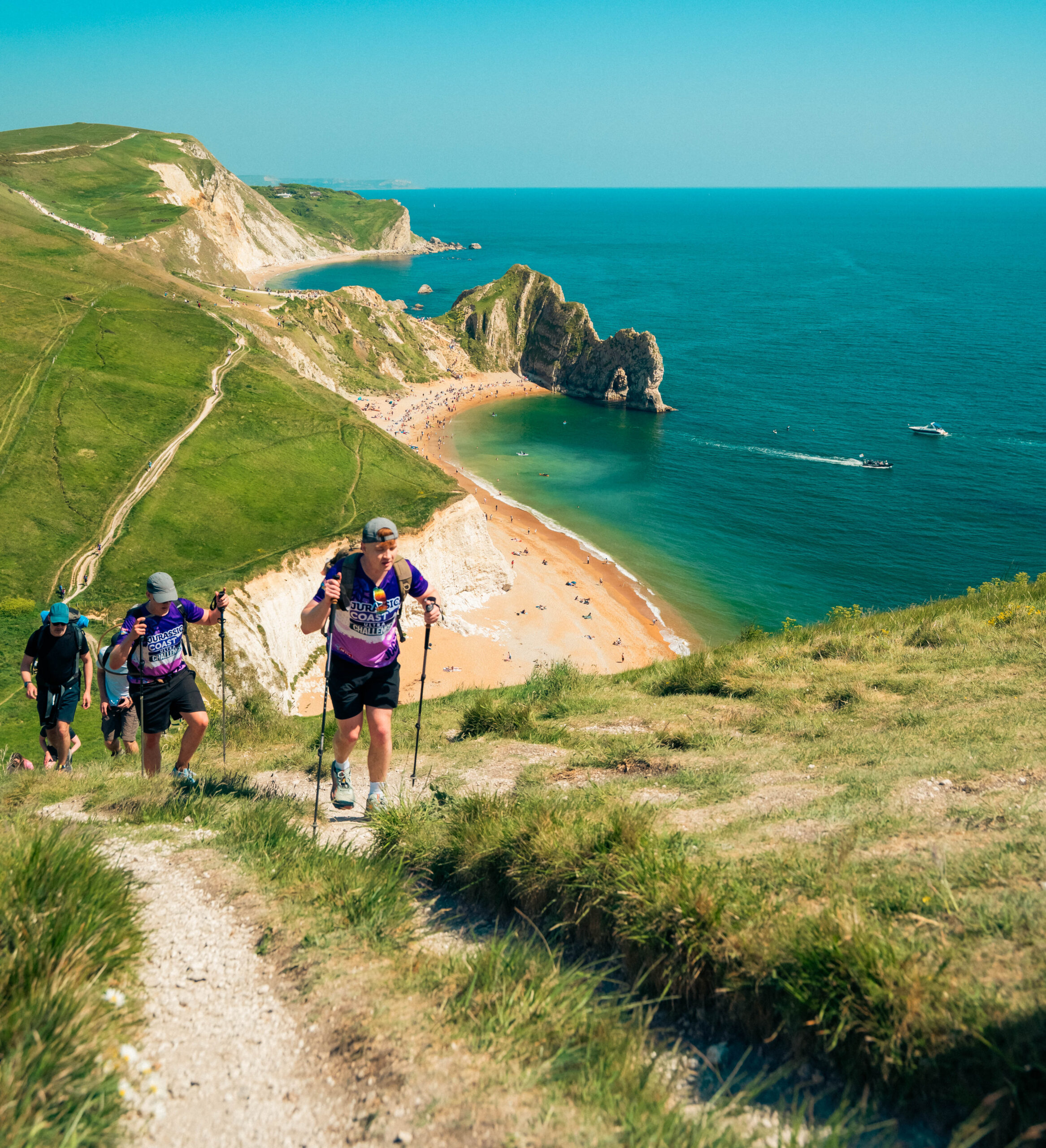 People make their way up a hill next to a cliff, with the sea in the background.