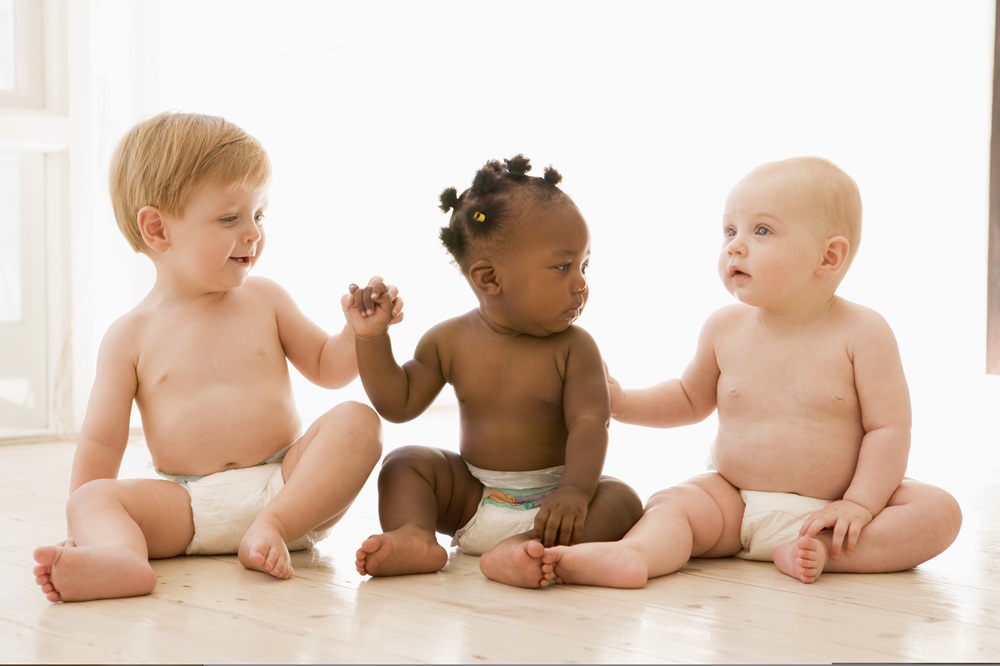 Three babies in nappies sitting on the floor and holding hands