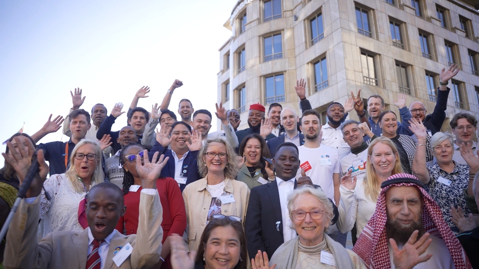 Four rows of CoMO members waving and smiling at the camera