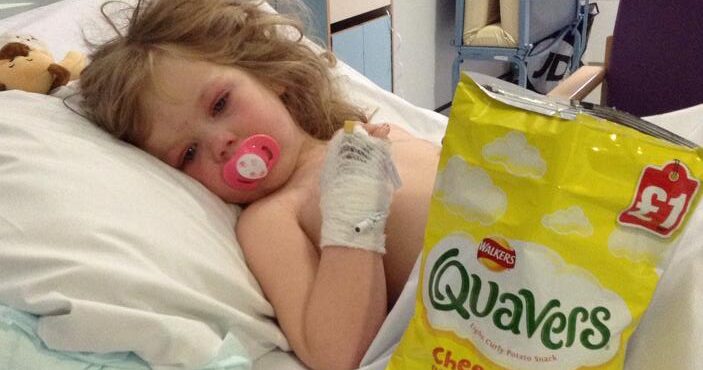 A photograph of Eloise Carter in a hospital bed with a large bag of crisps