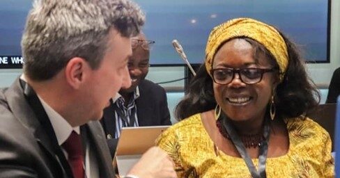A man and a woman having a conversation at a conference. The man is gesticulating and the woman is smiling at him.