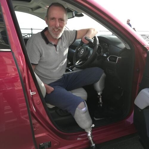 Photo of Mike Davies, sitting in the front seat of his car wearing prosthetic legs.