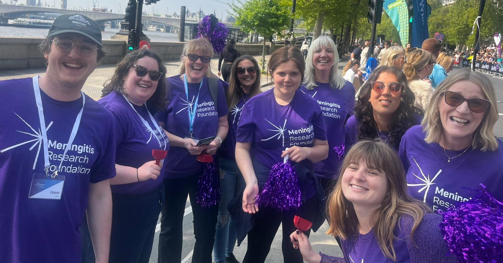 Nine people wearing Meningitis Research Foundation t-shirts smiling and holding pom poms