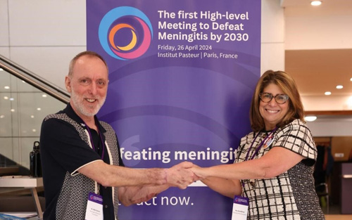 A man and a woman standing on either side of a pull-up banner sign clasping hands. The banner reads 