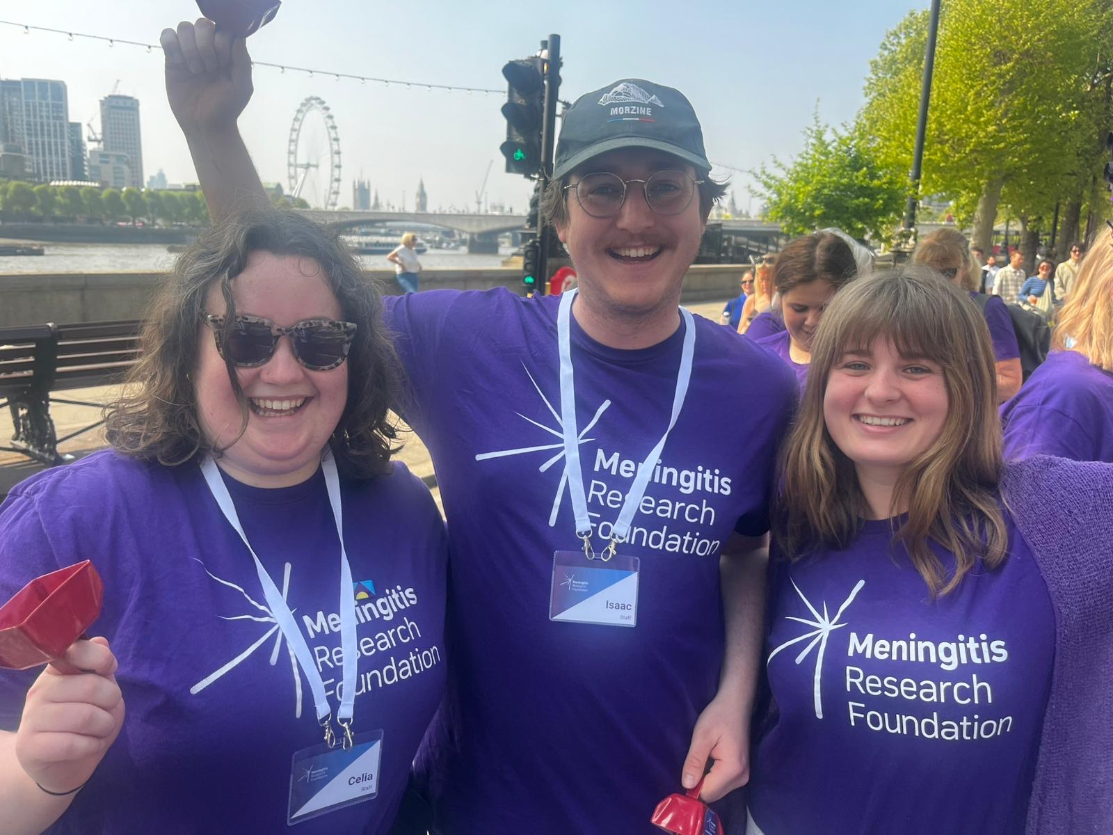 Three people wearing Meningitis Research Foundation t-shirts smiling.