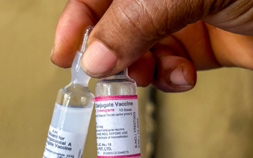 A hand holding two bottles of vaccines.