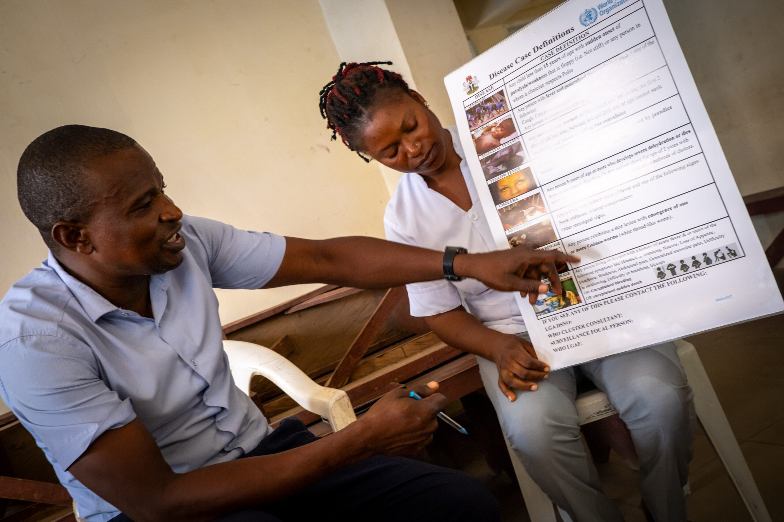A woman holds a poster with health information while a man points to the meningitis section of the poster.