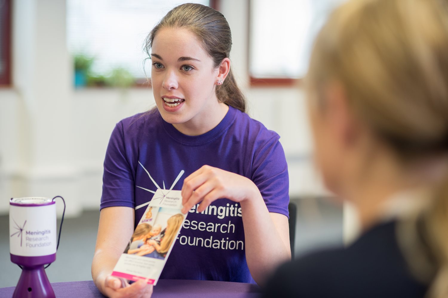 A woman in a Meningitis Research Foundation t-shirt holding up an information leaflet.