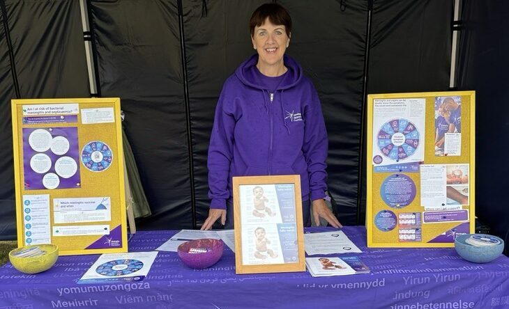 Woman wearing purple stood behind a stall with a purple table cloth and various materials on the table.