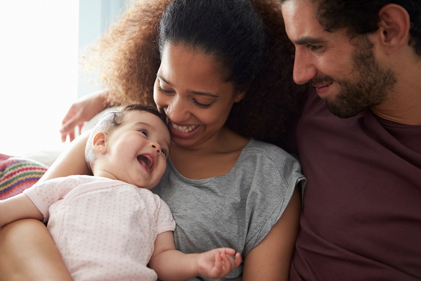 A woman and a man sitting on a sofa holding a smiling baby.