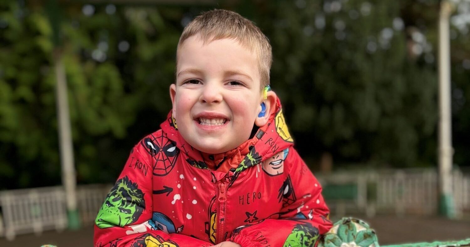 Arthur Kilcran smiling wearing a superhero coat and a hearing aid.