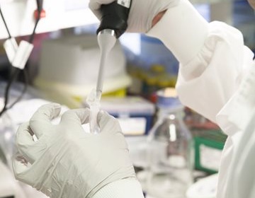 A pair of gloved hands holding a pipette in a lab.