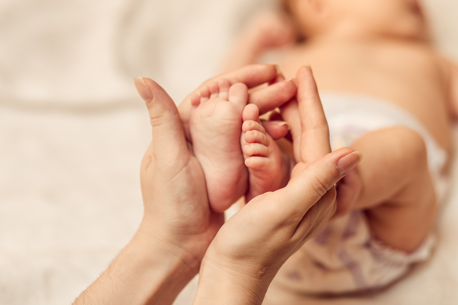A pair of adult hands holding a baby's feet.