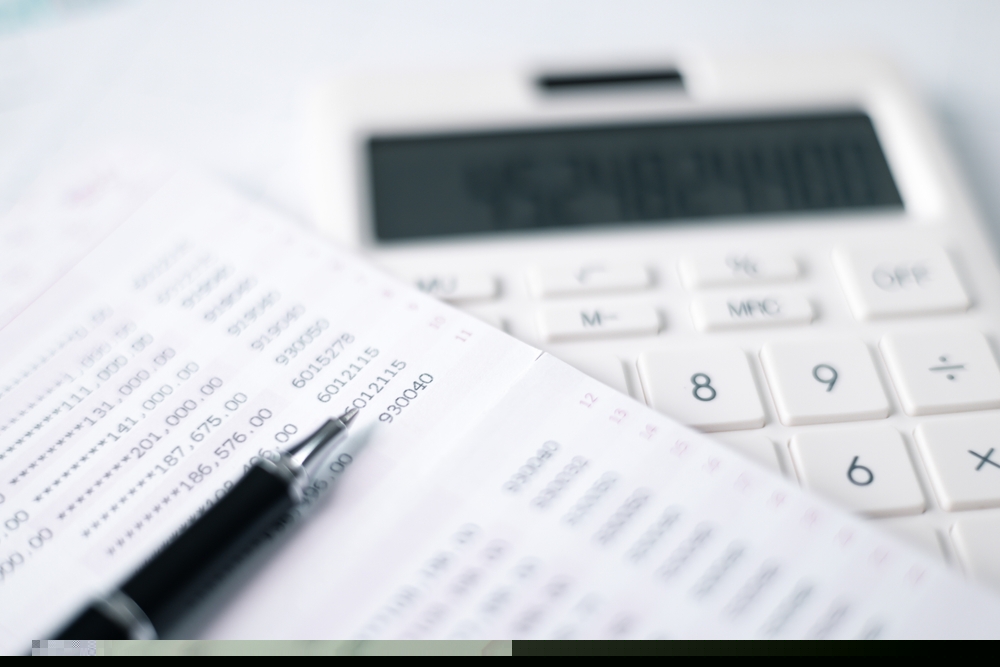 An accounts sheet, a pen and a calculator on a table.