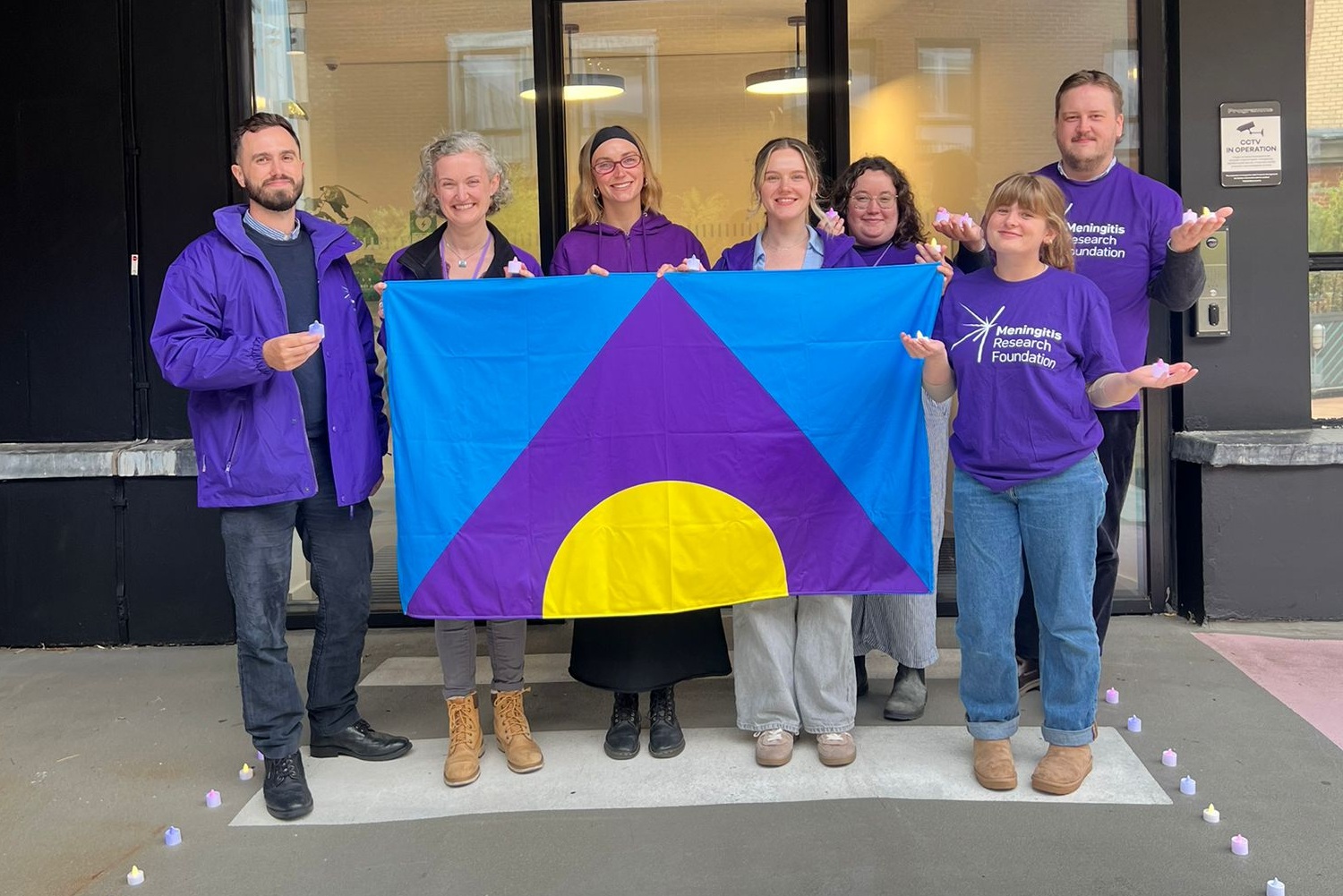 Six people in Meningitis Research Foundation t-shirts holding the Meningitis Flag.