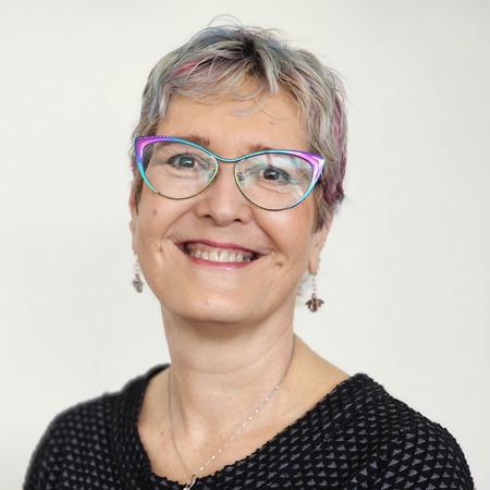 A headshot of Jane Plumb, a woman with short hair which has purple highlights, and wearing glasses with colourful frames.