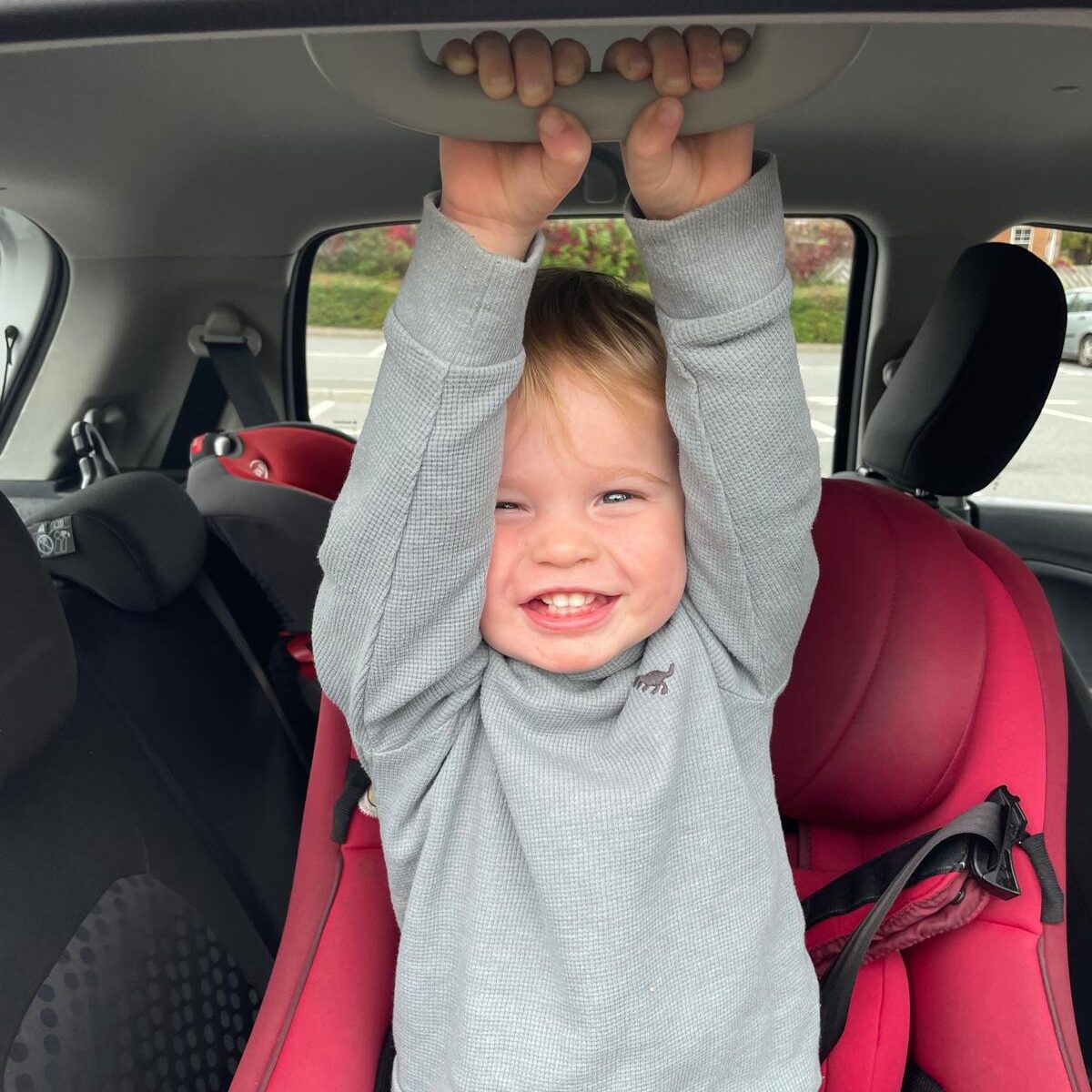 A young boy smiling whilst sat in a car seat