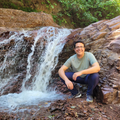 Herbert Cruz smiling sat next to a small waterfall.