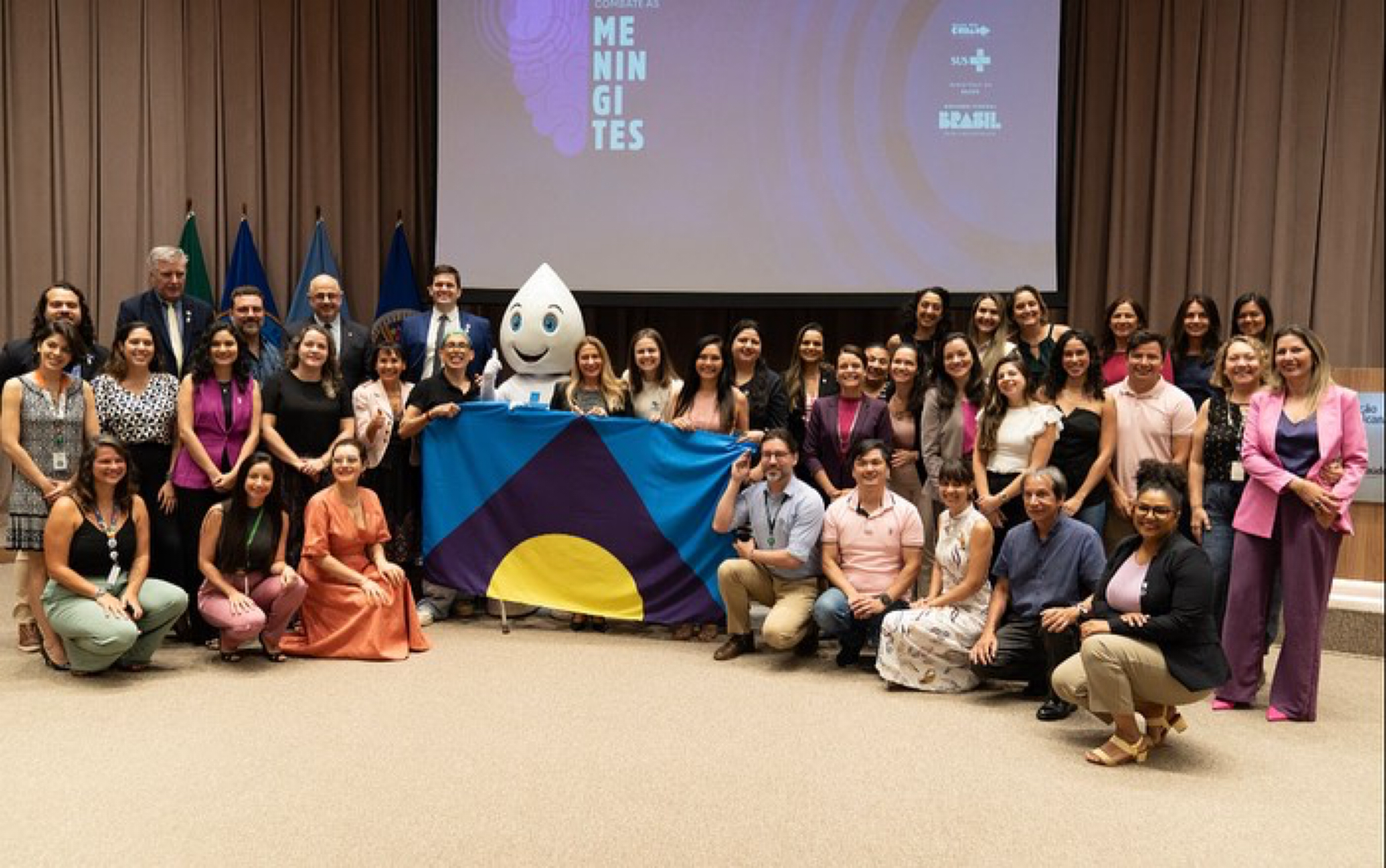 A large group of people in a conference room standing around the meningitis flag