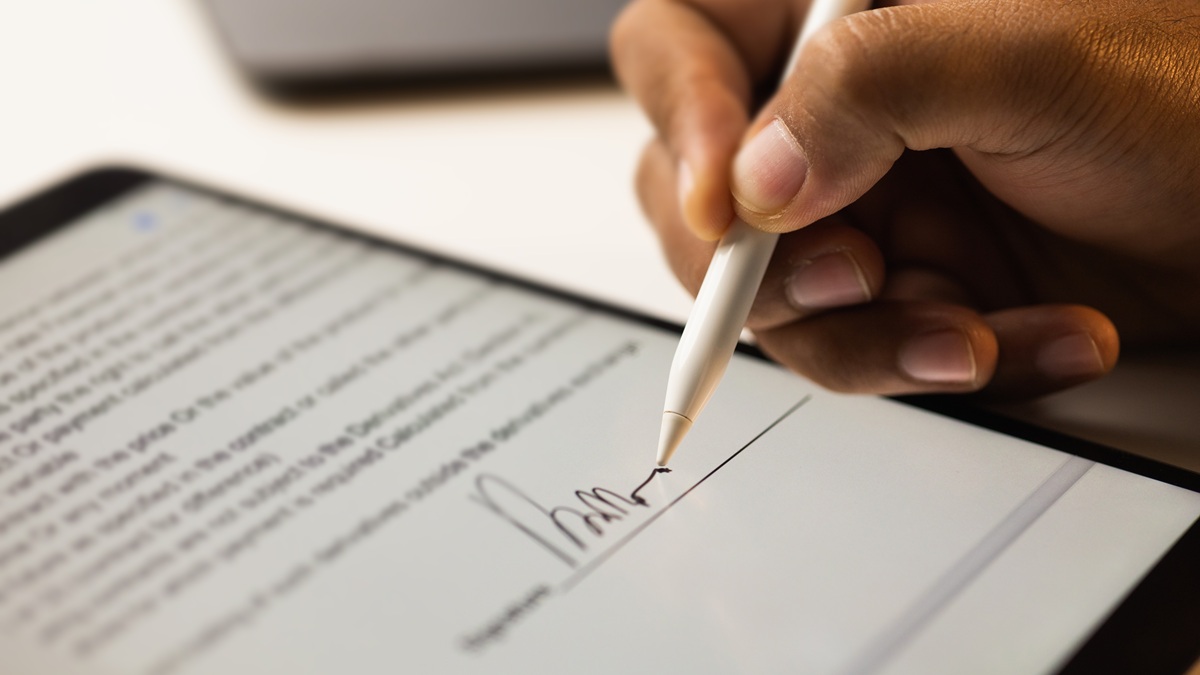 A hand signing a contract on a tablet using a stylus.