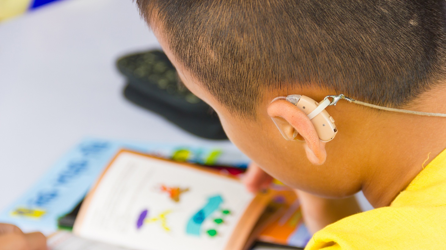 A boy with a hearing aid reading a book.