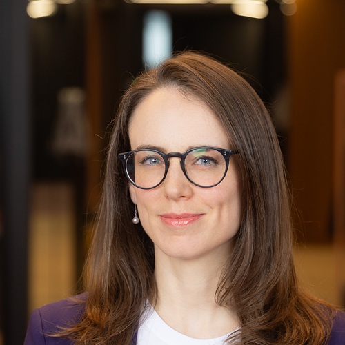 A woman with brown hair and black-rimmed glasses smiling.