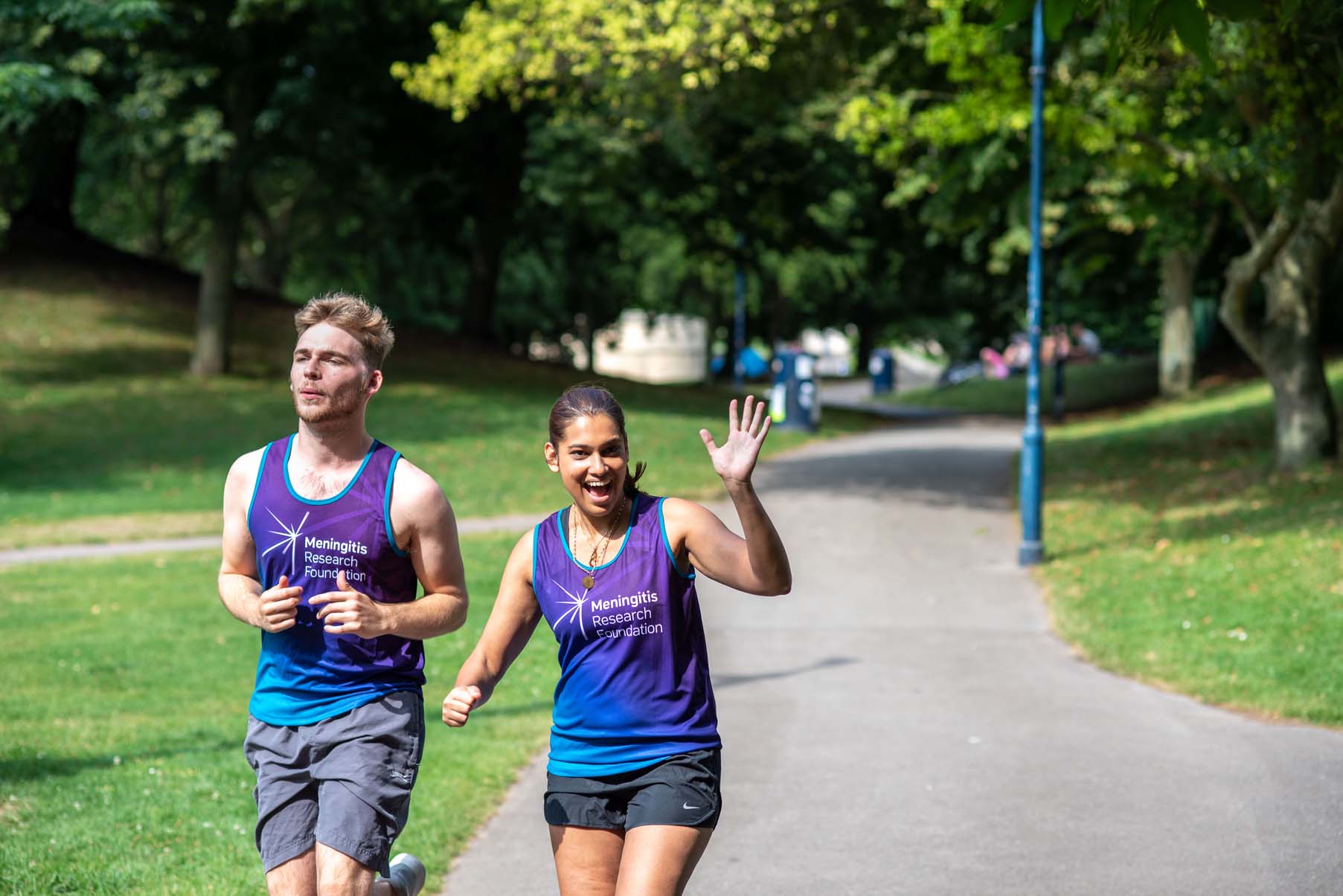 Two people in Meningitis Research Foundation vests run through a park.